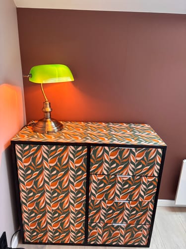 Customer's kommode dekket med Boho Leaves kontaktplast i et bladmønster med grønne og varme toner, toppet med en lampe.
