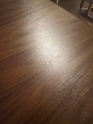 Reviewer's nærportrett av overflaten på Walnut Deep kontaktplast med synlig trestruktur og en liten ripe.
