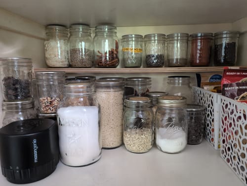 Customer's black Mason Genie vacuum sealer beside glass mason jars filled with spices in a pantry cupboard.