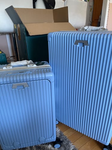 Customer's two blue All-in-One Carry-On suitcases next to an open cardboard box indoors.