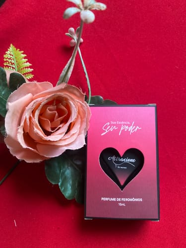 Customer's box of Perfume Attracione Sensual with a heart-shaped cutout, placed next to a soft pink flower on red fabric.