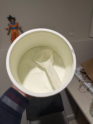 Customer's UGLYFACE AMINOS+ white plastic tub open with a scoop inside, held in a hand.