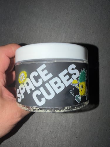 Kundenfoto der THC Space Cubes Dose, gehalten in einer Hand, mit gut sichtbarem Etikett und Ananas-Cartoon.