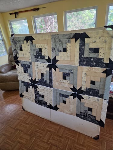 Reviewer's Maggie's Cabin quilt top in progress, featuring blue and cream log cabin blocks with star accents.