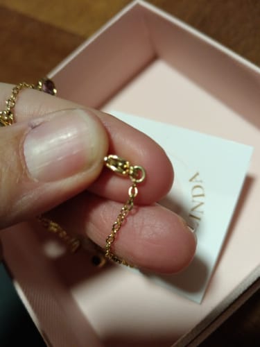 Customer's hand holding the gold-plated chain and charm of the Collana con ciondoli pendenti colorati.