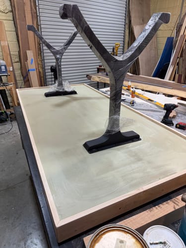 Customer's black Wishbone furniture legs wrapped in plastic, positioned on a large wooden tabletop in a workshop.