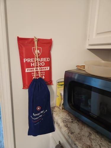 Customer's blue NovaCare Emergency Access Pouch hanging on a wall next to a fire blanket in a kitchen.