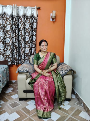 Customer's pink and green Aurelia Royale Crepe Khaddi Silk Saree with zari work, worn by a person sitting on a sofa.