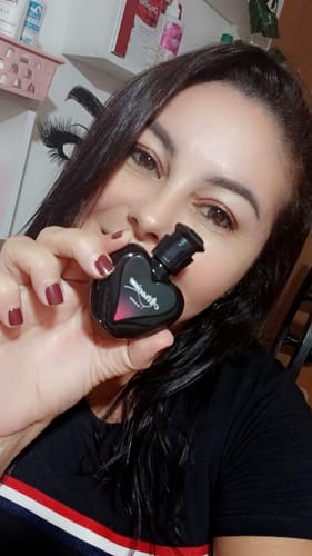 Customer segurando o frasco em formato de coração do perfume Attracione Sensual próximo ao rosto.
