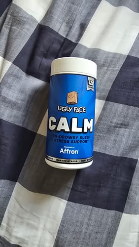 Customer's blue bottle of UGLYFACE CALM supplement, sitting on a gray and white checkered fabric.