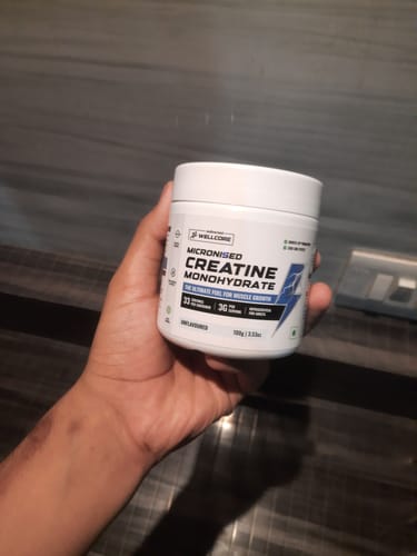 Reviewer's hand holding a white, round jar of Wellcore Micronised Creatine Monohydrate.