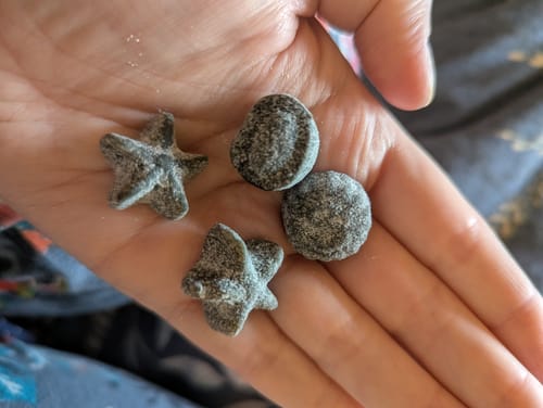 Customer's hand holding four dark, unique shapes of Swedish Salty Liquorice Mix.