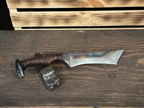 Customer's custom metal knife with a smooth, finished blade sitting on a dark wooden surface.
