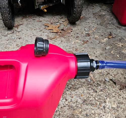 Customer's red 5 Gallon Jug with wide cap and blue fill hose attached on a paved surface.