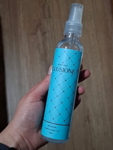 Customer's hand holding the blue, cylindrical Illusione body splash bottle.