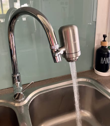 Customer's silver BlissfulHome kitchen tap filter attached to a sink faucet, dispensing water.