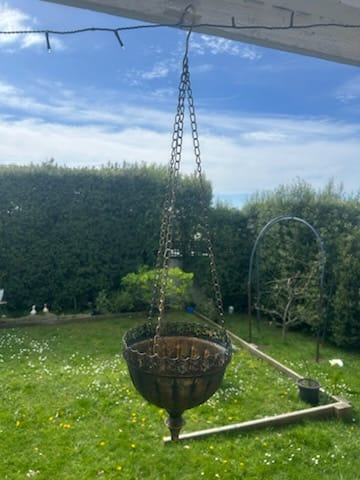 Customer's Naxos hanging planter with aged gold finish hanging in a garden setting