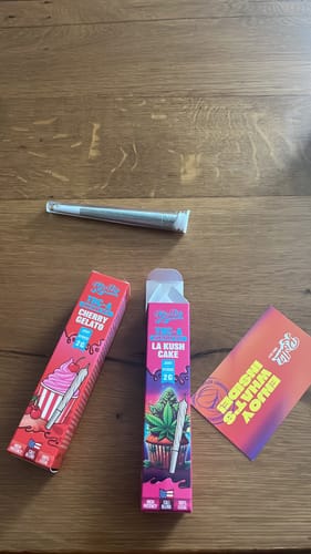 Customer's THC-A Pre-Roll Cali Blend items, including two colorful boxes and a single cone on a wooden table.