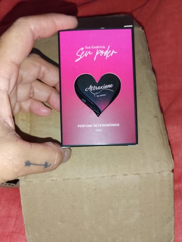 Customer's hand holding the Perfume Attracione Sensual box with a heart-shaped cutout against a box packaging.
