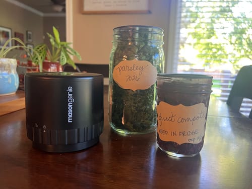 Customer's Mason Genie vacuum sealer beside two labeled mason jars containing dried parsley and fruit compote.