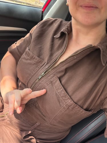 Reviewer wearing the umber Lagoon Suit with a front zip, making a peace sign while sitting in a car.