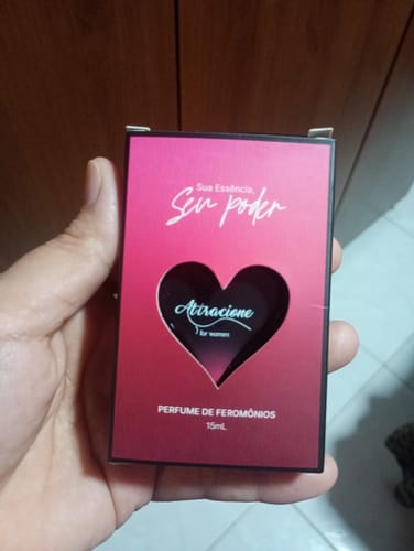 Customer's hand holding the box for Attracione Sensual perfume, featuring a red gradient and a heart-shaped cutout.