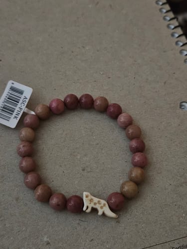 Customer's pink beaded Ascent bracelet featuring a small, detailed snow leopard emblem on a textured surface.