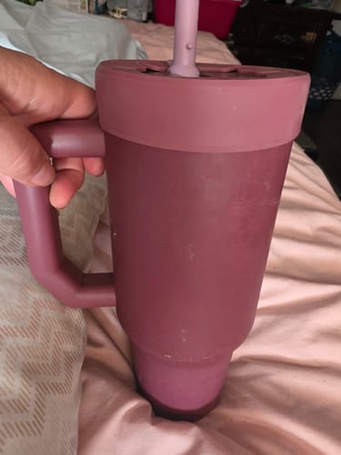 Customer's hand holding a mauve Thicc Buddy 40oz cup with a straw lid in a bedroom setting.