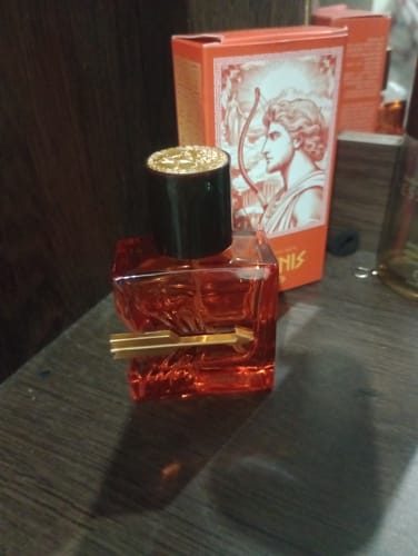 Customer's Adonis Zayed perfume bottle in orange, with golden arrow detail and matching box in the background.