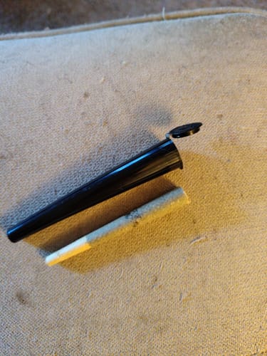 Customer's California Gold Hash Hole pre-roll lying next to an open black plastic carrying tube.