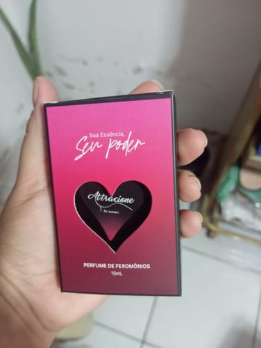 Customer's hand holding the box of the Attracione Sensual perfume, featuring a pink and black heart design.