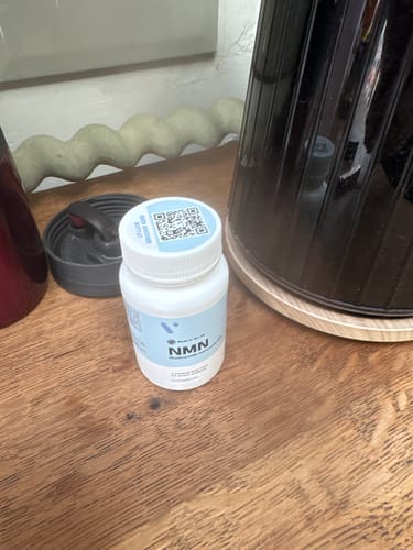 Flacon blanc de gélules NMN 500 mg de la cliente posé sur une surface en bois à côté d'un appareil foncé.