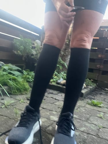 Customer's black Støttestrømper worn while running outdoors, showing a secure fit on the legs.