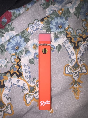 Customer's orange Rollz THCA vape pen with a pink cap, resting on a floral fabric surface.