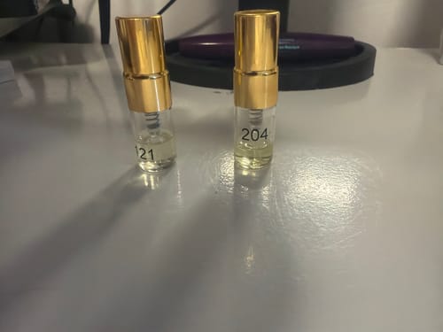 Customer's Tester Set with two small glass perfume vials numbered 121 and 204 with gold caps on a surface.