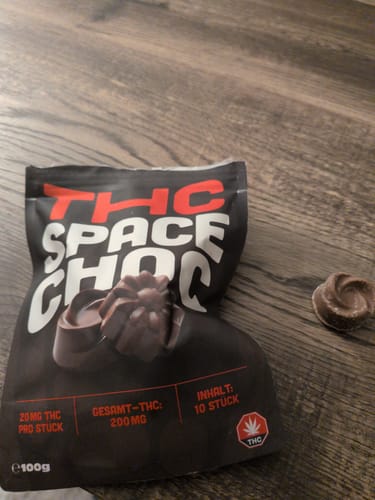 Kundenfoto der THC SpaceChoc Packung mit einer einzelnen, kleinen, braunen Schokoladenpraline auf einer Holzoberfläche.