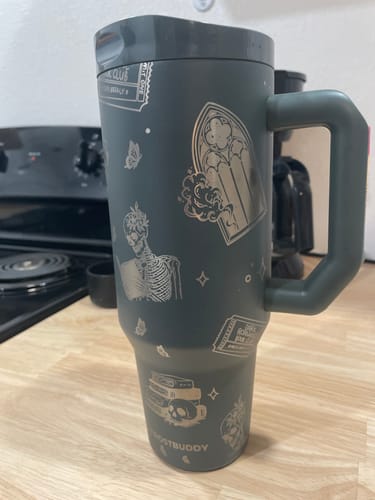 Customer's grey Thicc Buddy 40oz mug featuring detailed occult and skeleton etchings, sitting on a kitchen counter.
