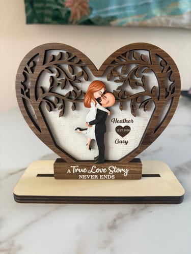 Customer's personalized wooden heart plaque featuring a couple kissing under a tree, displayed on a wooden stand.