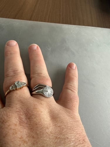 Customer's rings on hand, featuring one thin band with a light gemstone and a wider, sunburst-patterned silver ring.