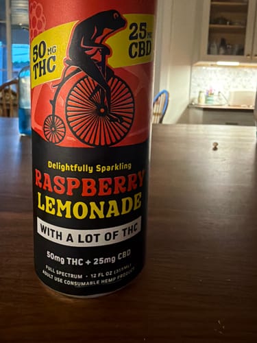 Customer's Sparkling THC Raspberry Lemonade can showing frog on penny-farthing logo, standing on wooden table.