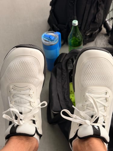 Customer's white CUURT Muuv court shoes with wide toe boxes worn on feet, with a gym bag and water bottle nearby.