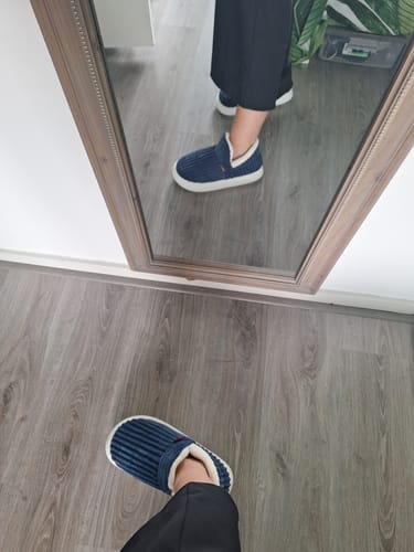 Reviewer's feet wearing blue ribbed HappyCozy slippers with thick white soles, seen in a mirror reflection.