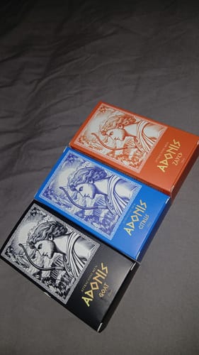 Customer's three Kit Adonis perfume boxes in orange, blue, and black displayed together on a grey surface.