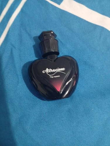 Customer's Attracione Sensual perfume, a black heart-shaped bottle on a blue fabric background