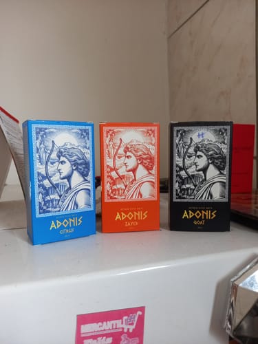 Reviewer's Kit Adonis perfume boxes in blue, orange, and black, displayed on a counter.