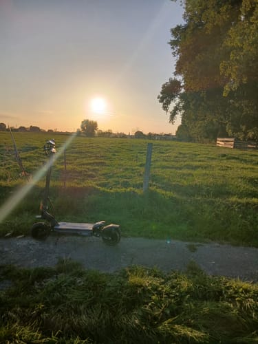 Customer's Ausom Gosoul 2 Pro electric scooter parked on a path in a green field during sunset.