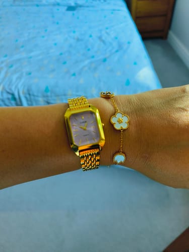 Reviewer's gold Claire De Mains watch with a light face worn on a wrist alongside a gold flower bracelet.