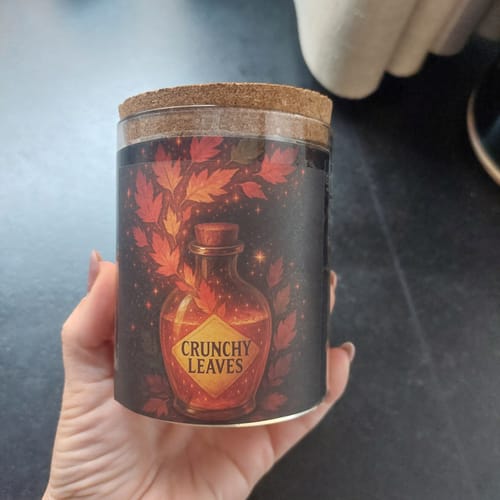 Reviewer's hand holding a round tea tin labeled Crunchy Leaves featuring autumn leaf graphics.