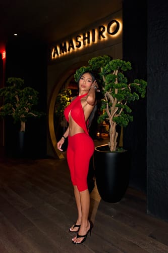 Customer's red Carmen Wrap Capri worn as a halter-style outfit while standing at night by an illuminated restaurant sign.