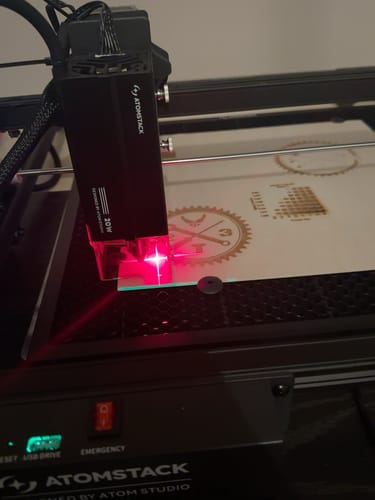 Customer's AtomStack A20 Pro V2 laser engraver working on wood, showing the laser head emitting a bright red light.